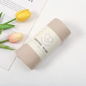 Beige katoenen sjaal in rolvorm met papieren wikkel en bloemdecoratie op een witte basis