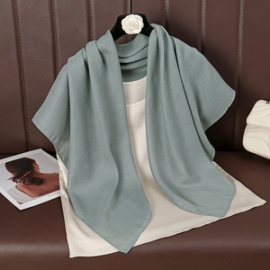 Detail of sage green cotton linen scarf with fine diagonal texture on a coat hanger
