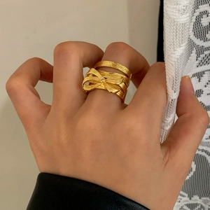 Golden bow knot ring with crystal center and multi-layered textured band on finger