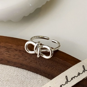 Détail d'une bague nœud argentée ajustable sur un fond en tissu rustique