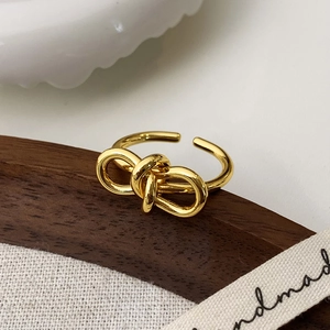 Vue détaillée d'une bague nœud dorée polie sur un support en bois et tissu en lin