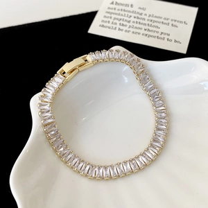 Nahaufnahme eines goldenen Tennisarmbands mit rechteckigen Zirkonen auf Keramik
