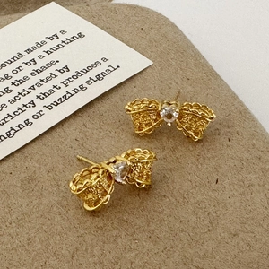 Macro detail of gold bow-knot earrings with lace texture and heart zircon stone