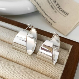 Macro detail of silver mirror-polished thick hoop earrings in a wooden jewelry box