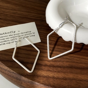Détail de boucles d'oreilles losanges argentées avec fini mat texturé sur bois