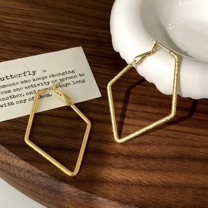Vue détaillée de grandes boucles d'oreilles losanges dorées avec une finition mate