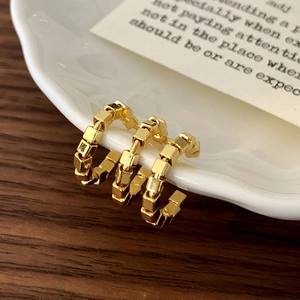 Macro detail of golden geometric cube beaded hoop earrings on a ceramic display