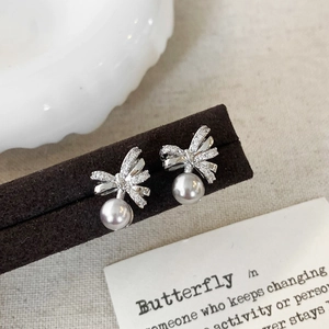 Detailed view of silver bow earrings with micro-set zircon and dangling pearl beads