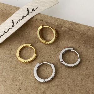 Détail macro de boucles d'oreilles créoles dorées et argentées serties de zircons blancs