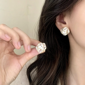 Elegant gold hollow flower earrings with white texture worn by a model in close-up