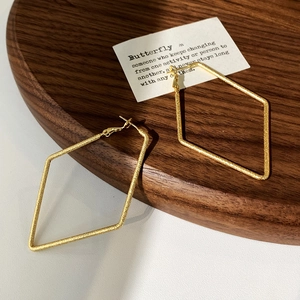 Vue détaillée des boucles d'oreilles losanges avec texture dorée brossée sur plateau bois