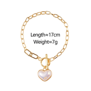 Dettaglio del bracciale a catena dorata con chiusura OT e ciondolo a cuore bianco