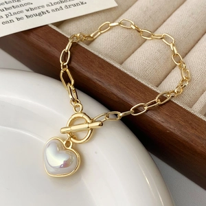 Dettaglio del bracciale dorato con ciondolo a cuore, chiusura a T e fascino perlato