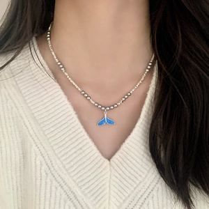Elegant silver bead necklace with a blue enamel whale tail pendant on a white sweater