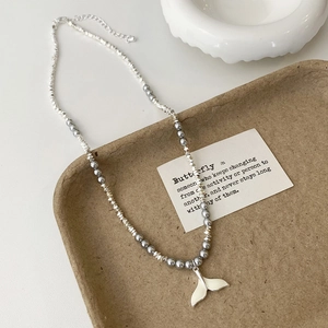 Close-up of pearl and silver bead necklace with a white fishtail pendant on a tray