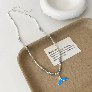 Detail of blue fish tail pendant necklace with silver beads and grey pearls on a tray
