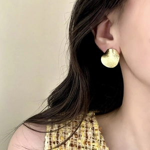 Golden round stud earrings with woven texture worn by model for high-end fashion look