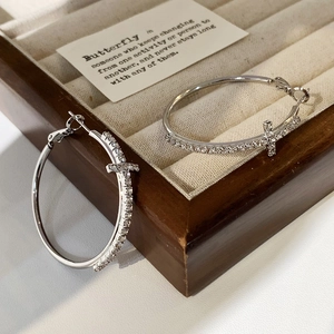 Detailed close-up of silver hoop earrings with sparkling zircon cross pendants in a jewelry box