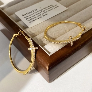 Detailed close-up of gold hoop earrings with sparkling cubic zirconia cross pendants