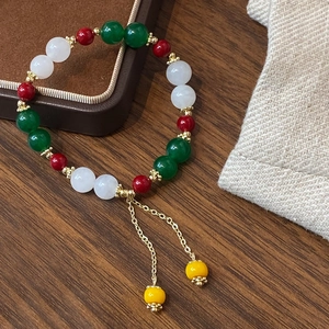 Dettaglio del bracciale in perle di giada multicolore con nappe dorate su legno