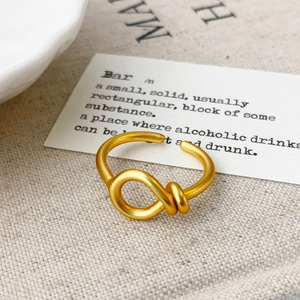 Minimalist matte gold knot open ring displayed on an elegant aesthetic background