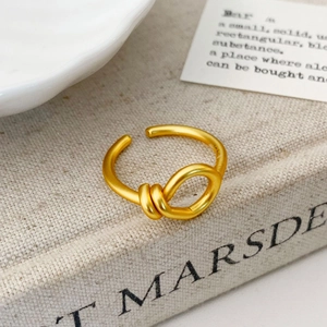Close-up of golden matte knot ring on textured linen surface showing minimalist design