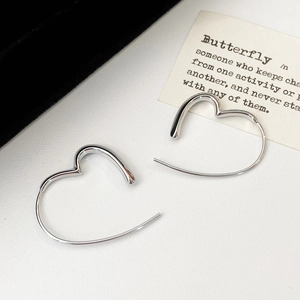 Detailed view of heart-shaped silver earrings with a polished mirror finish on white leather