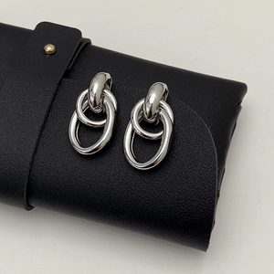 Polished silver nested ring earrings hung on a textured black leather pouch edge