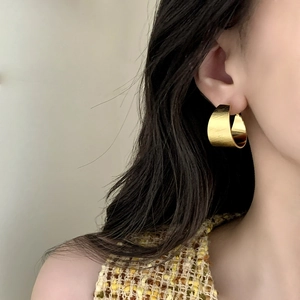 Orecchini a C minimalisti in oro spazzolato mostrati su una modella elegante