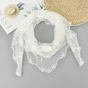 Détail d'une écharpe en dentelle blanche avec broderie florale et bords festonnés