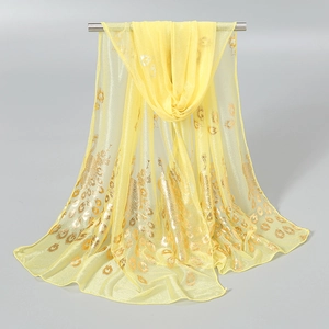 Detailed close-up of light yellow scarf featuring shiny golden peacock feather prints