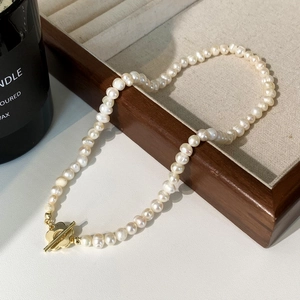 Détail d'un collier en perles d'eau douce avec fermoir à bascule doré sur plateau en bois