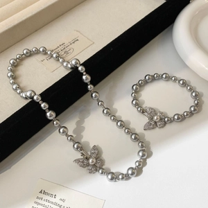 Détail du collier et bracelet en perles grises avec pendentif papillon en zircon
