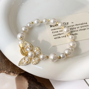 Vue détaillée du bracelet de perles avec pendentif papillon en cristal sur plateau céramique