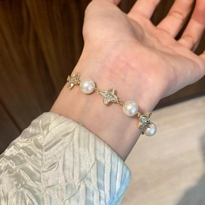 Elegant gold pearl bracelet with cubic zirconia clover charms worn on a woman's wrist