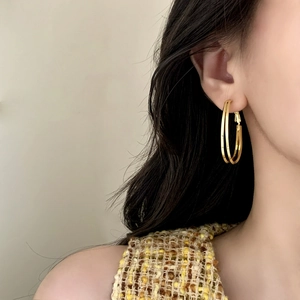 Gros plan d'élégantes créoles doubles dorées portées par un mannequin en tweed chic