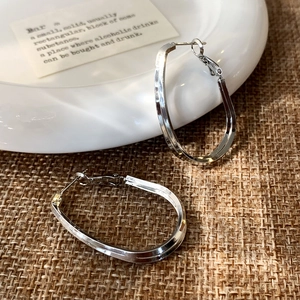 Détail macro de boucles d'oreilles créoles argentées superposées sur céramique et toile