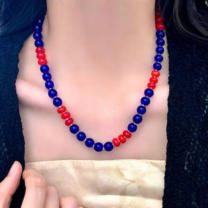 Detail of a handmade necklace featuring alternating dark blue and vibrant red glass beads