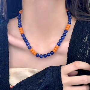 Detail of dark blue translucent beads and orange discs on stainless steel necklace