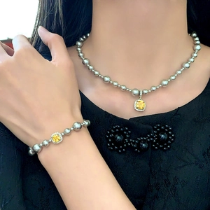 Détail de la parure de bijoux en perles argentées avec pendentifs carrés en pierres jaunes