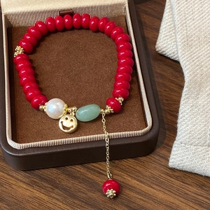 Macro shot of red beaded bracelet with pearl, green stone, and golden smiley pendant