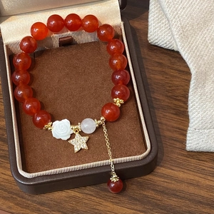 Nahaufnahme des Perlenarmbandes aus rotem Achat mit weißer Kamelie und goldenem Stern