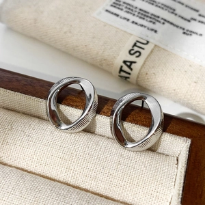 Macro shot of silver oval stud earrings with side engraved lines on a wooden jewelry box