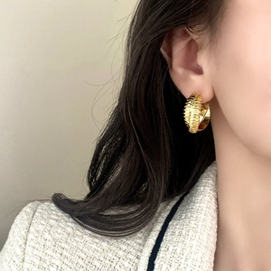 Eleganti orecchini a cerchio dorati a coste con design a strisce incrociate su una modella