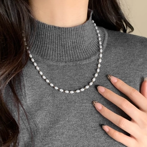Elegante Perlenkette im französischen Stil mit Goldkette auf grauem Strickpullover