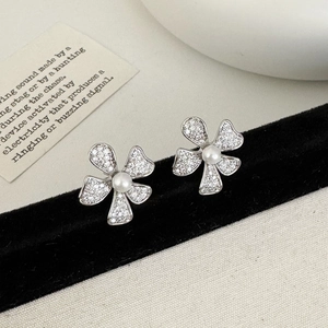 Détail macro de boucles d'oreilles fleur argentées avec zircons et perle centrale