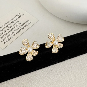 Détail macro de boucles d'oreilles fleur dorées avec zircon et perle blanche centrale