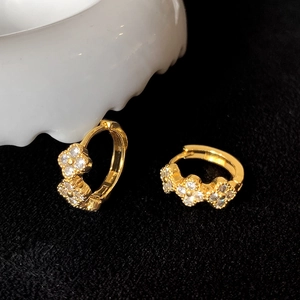 Macro d'oreillettes trèfles plaquées or serties de zircons brillants sur fond noir élégant
