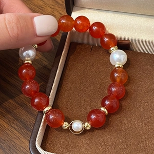 Elegant red agate bead bracelet with white pearls and gold accents on a jewelry box