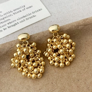 Détail de boucles d'oreilles pompon en perles dorées sur fond de papier texturé